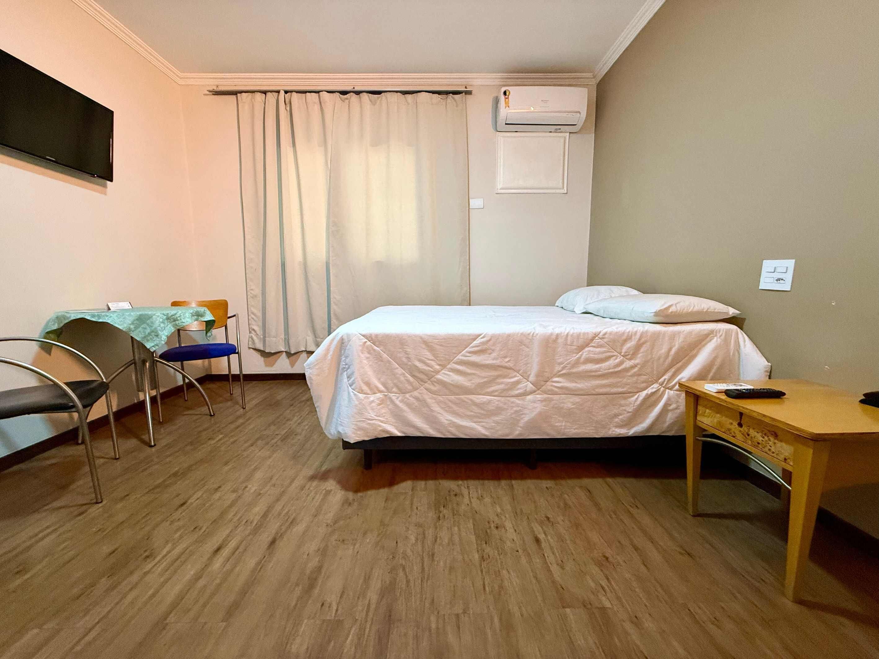 Una habitación de hotel con una cama, un escritorio, una silla, un aire acondicionado y una cortina.