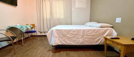 Una habitación de hotel con una cama, un escritorio, una silla, un aire acondicionado y una cortina.