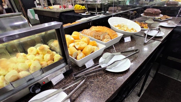 A buffet with various food items including bread, pastries, and a cake. - Granville Hotel (Curitiba)