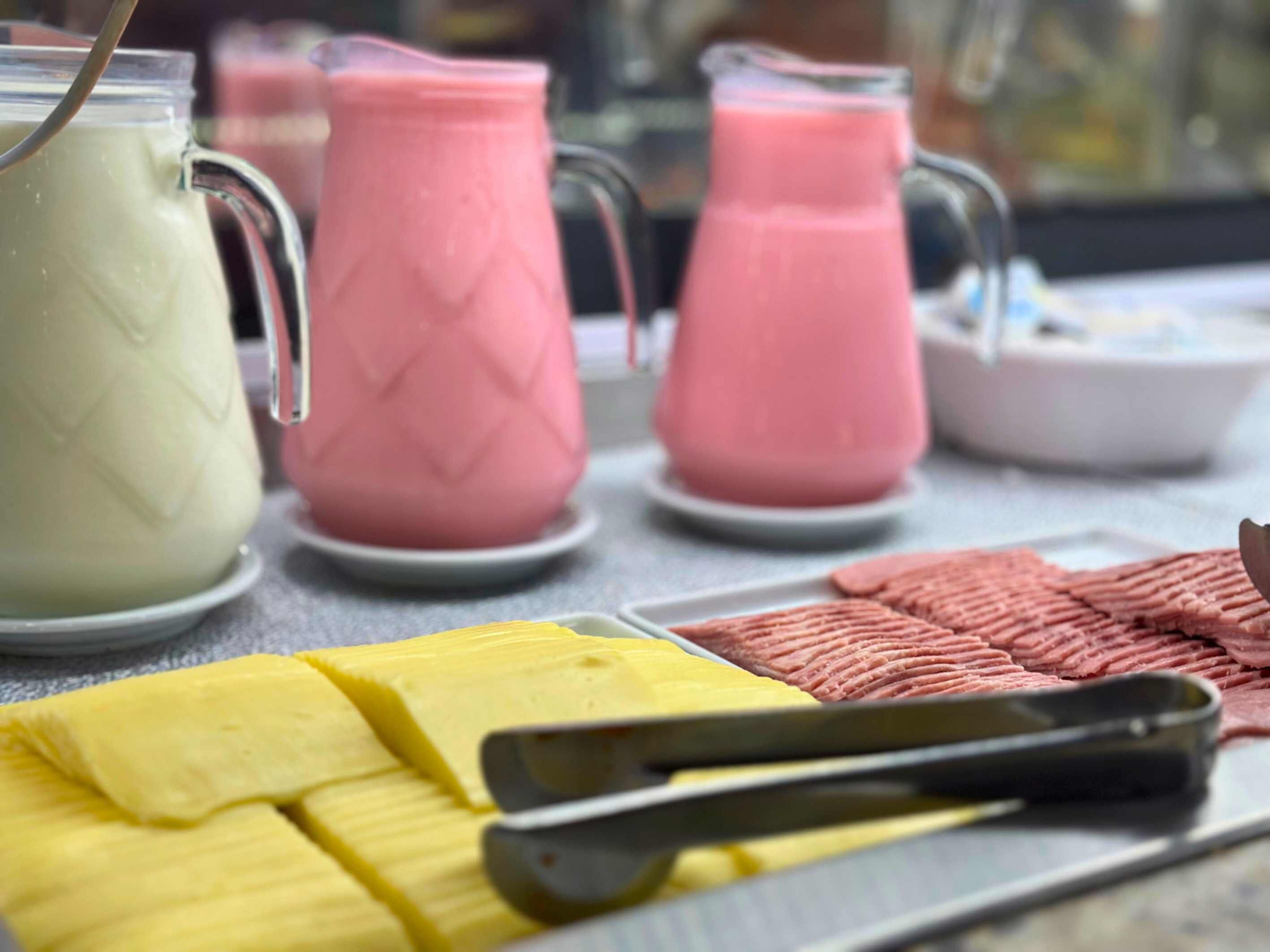 A table with a variety of food items and drinks, including a pitcher of a white beverage, a pink beverage, and a yellow food item.