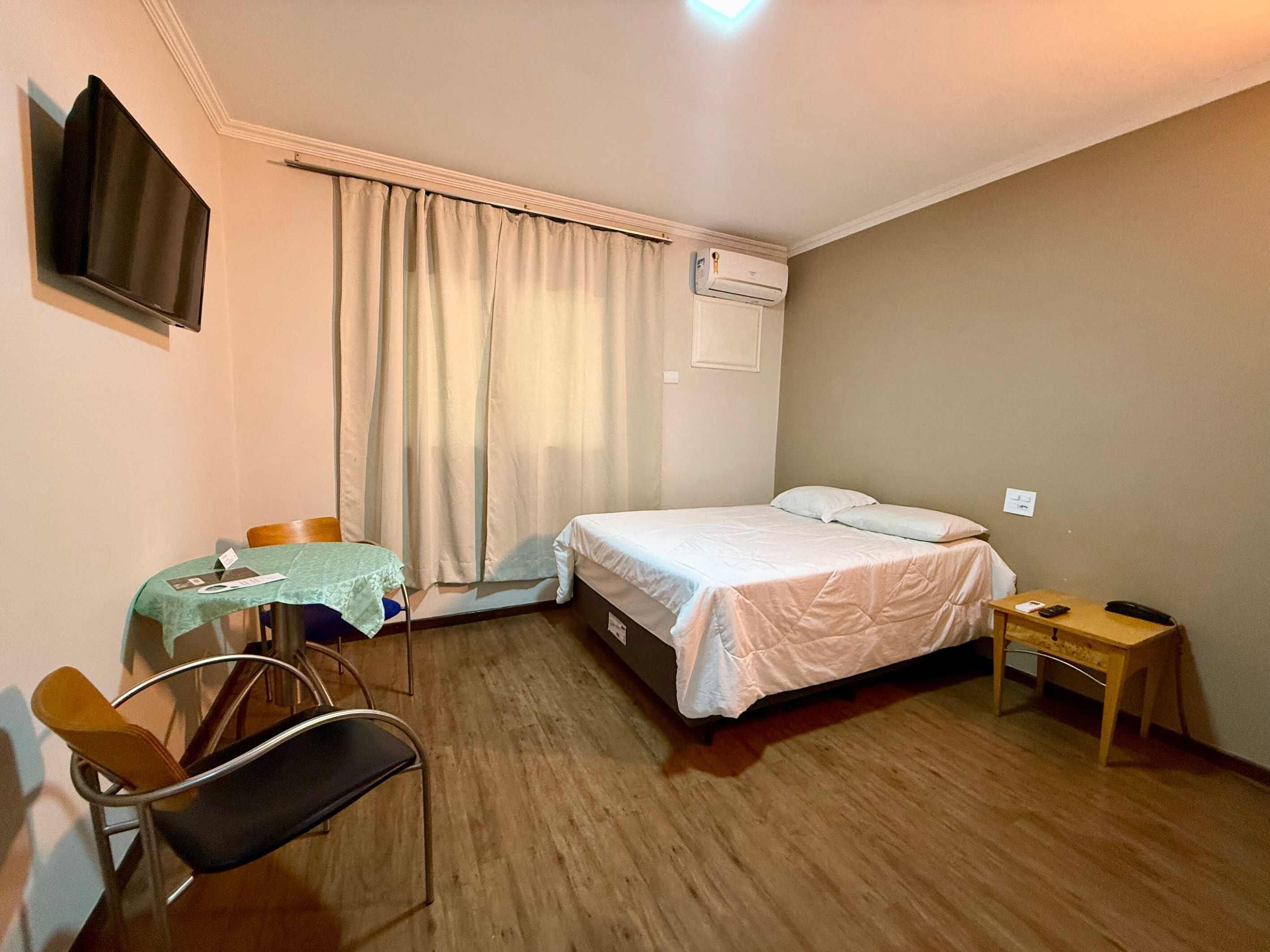 Een hotelkamer met een bed, een bureau, een stoel, een televisie en een airconditioning.