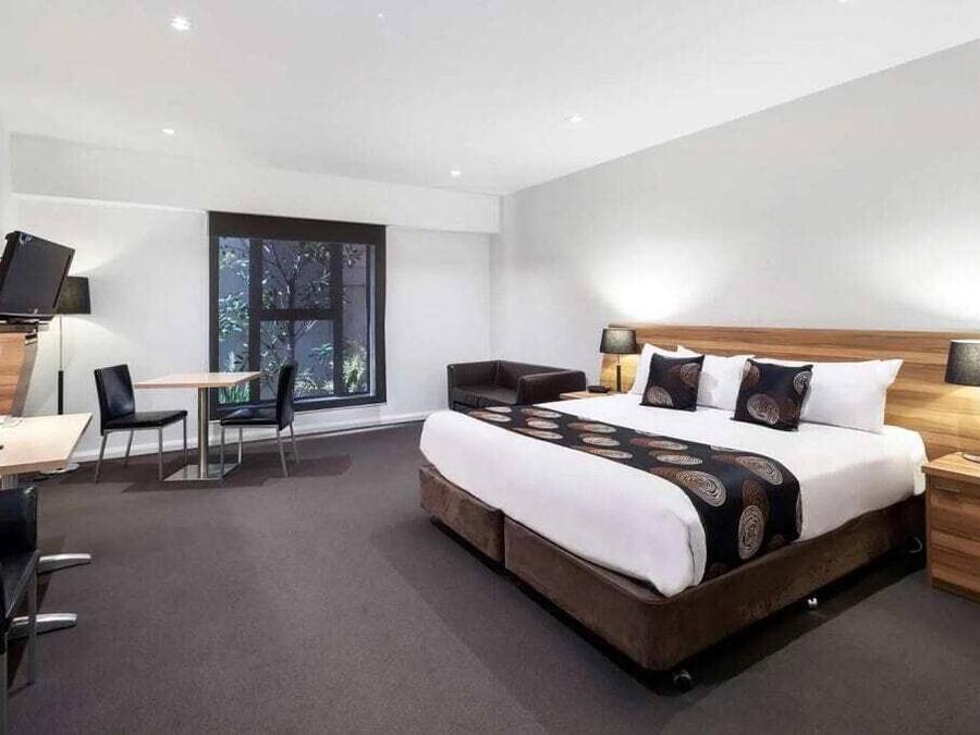 A modern hotel room with a large bed, a desk, a chair, and a TV.