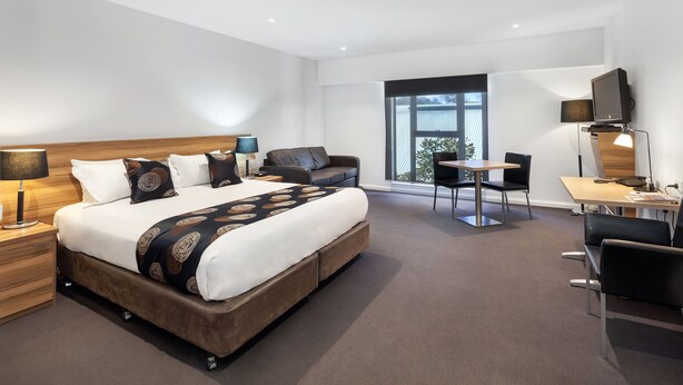 Una habitación de hotel moderna con una cama grande, un escritorio, una silla y un televisor.