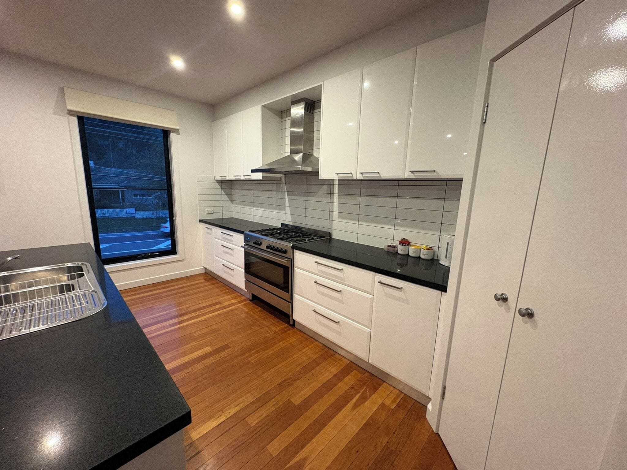 A modern kitchen with white cabinets, a black countertop, a stainless steel stove, and a window with a view of a street.