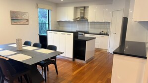 Una cocina moderna con armarios blancos, encimera negra y un comedor con mesa y sillas.