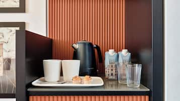Ein Frühstücksangebot mit einer schwarzen Kaffeemaschine, zwei weißen Tassen, einem Teller mit Muffins und zwei Milchkartons auf einer Tablett.