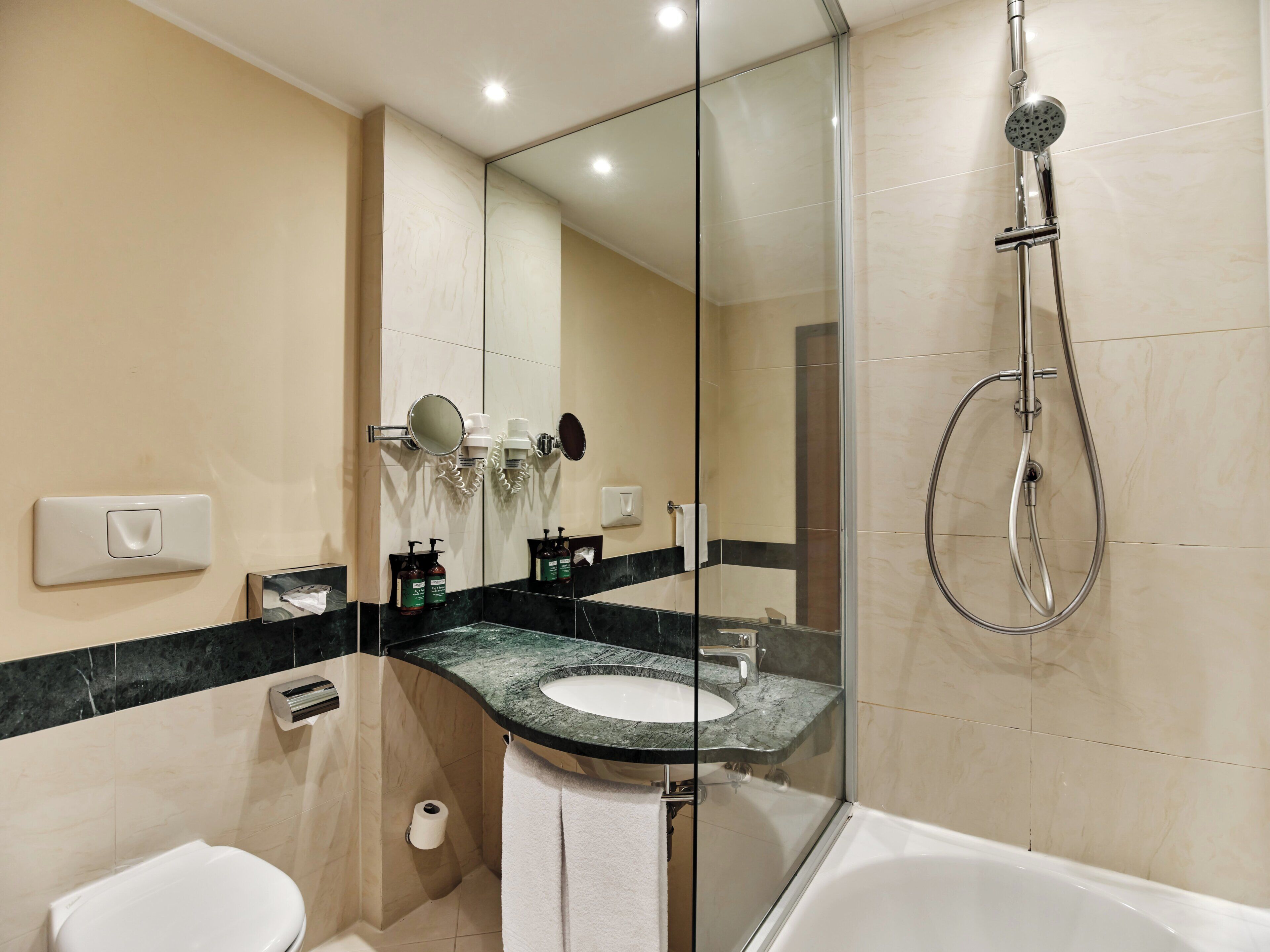 A modern bathroom with a glass-enclosed shower, a white toilet, a sink with a marble countertop, and a mirror.