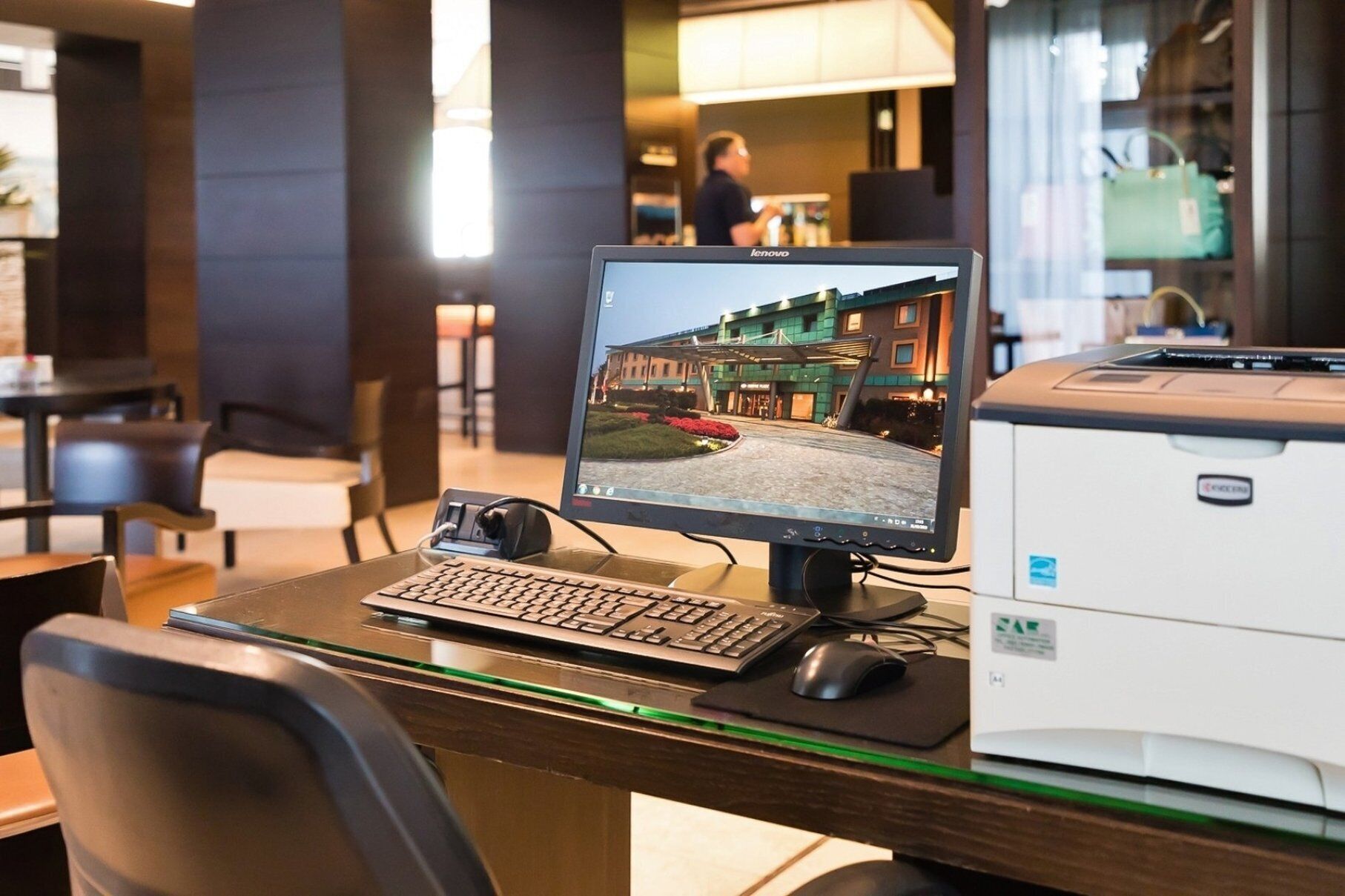 A hotel desk with a desktop computer, keyboard, mouse, and a printer.