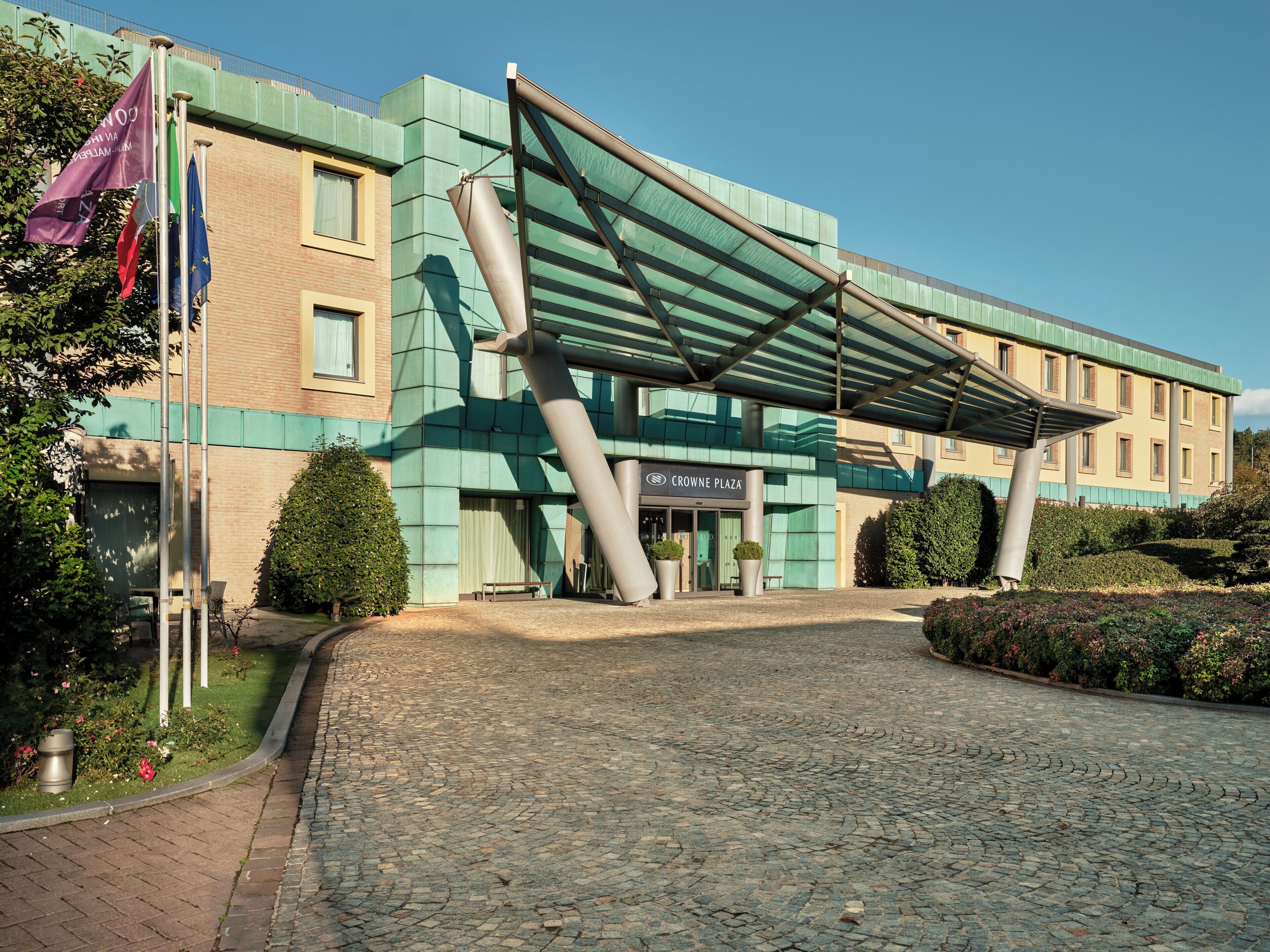 Entrada de hotel con un corredor cubierto, fachada de ladrillo y un letrero que dice 'CROWNE PLAZA'.