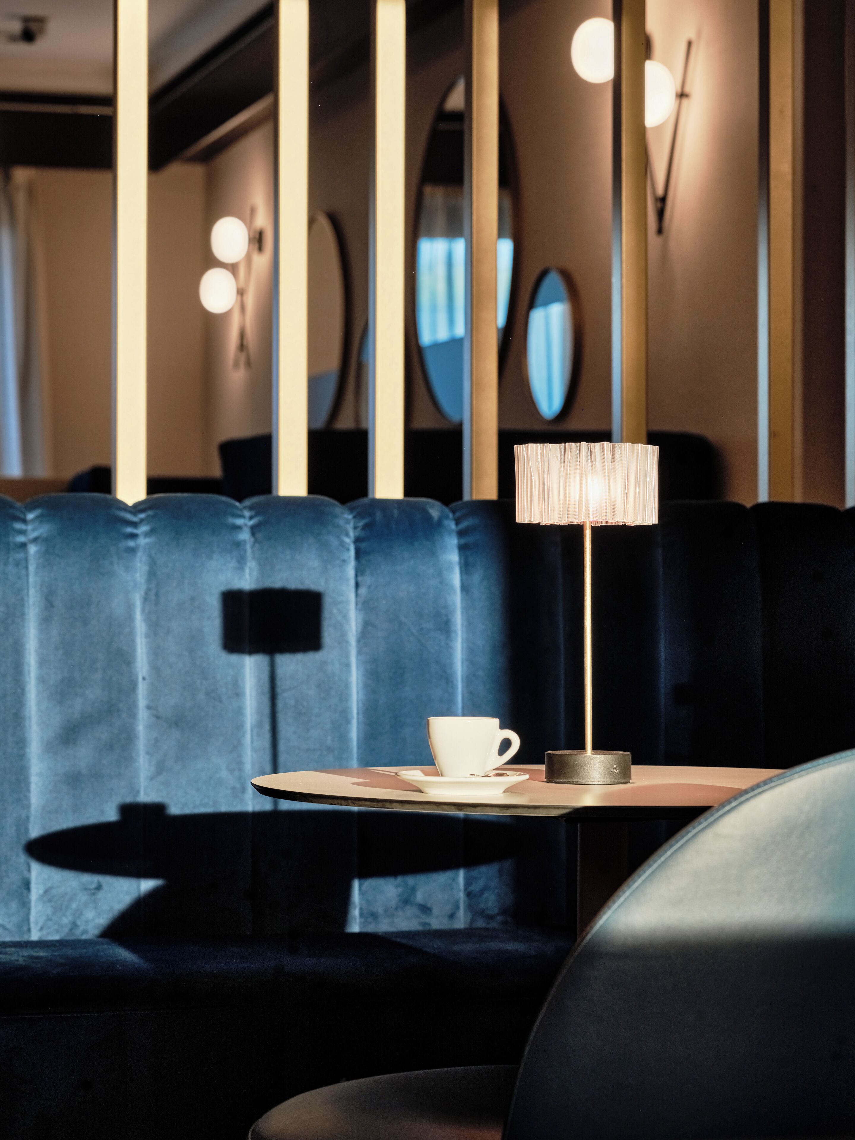 Un interior moderno con un banco tapizado en azul oscuro, una mesa con una taza y un plato blancos, y una lámpara de pie alta.