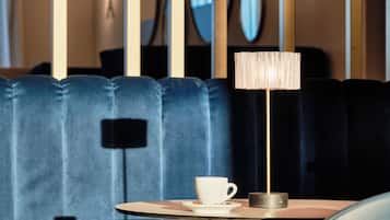 Un interior moderno con un banco tapizado en azul oscuro, una mesa con una taza y un plato blancos, y una lámpara de pie alta.
