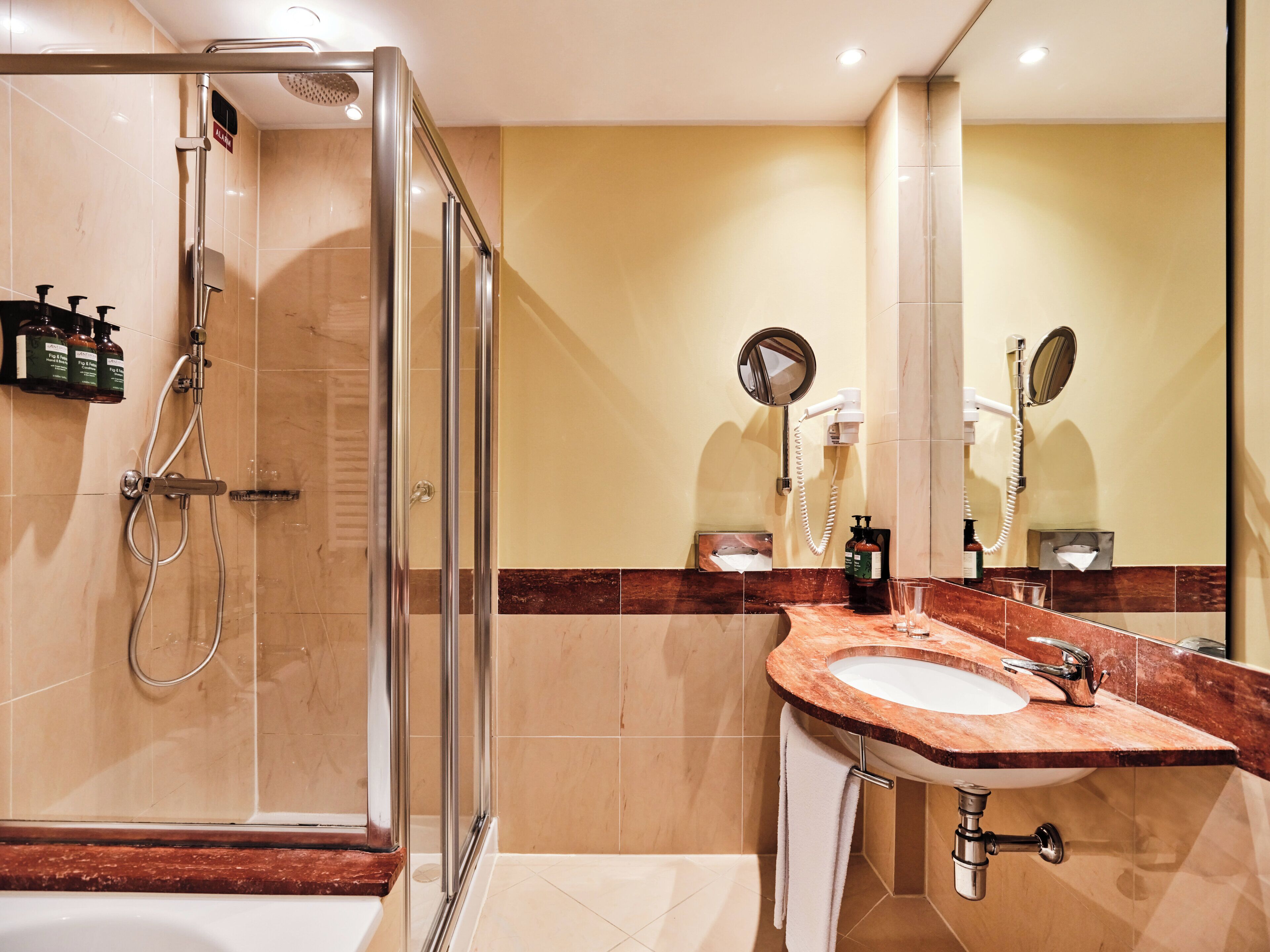 Een moderne badkamer met een douche met glazen wand, een marmeren wastafel en twee spiegels.