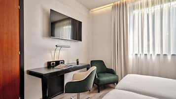 A hotel room with a bed, a desk with a chair, a television, and a window with curtains.