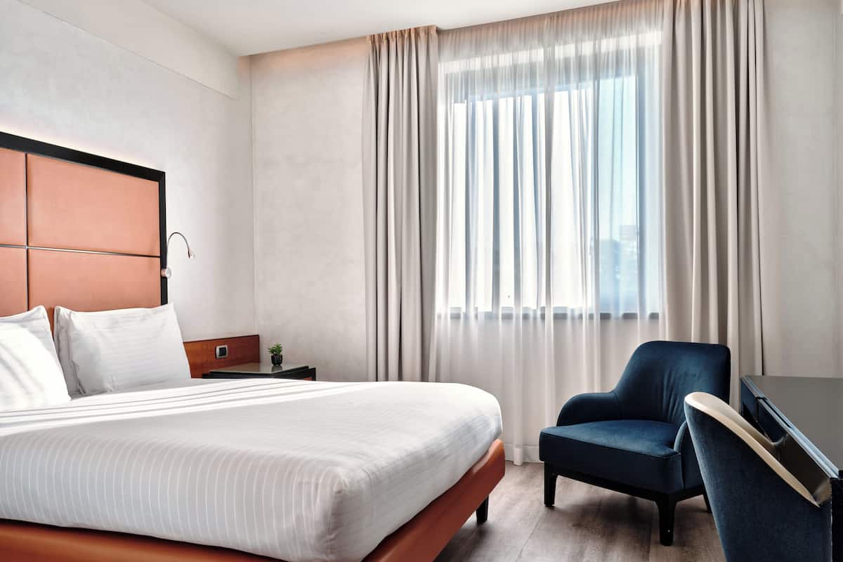 A hotel room with a bed, a desk, a chair, and a window with curtains.