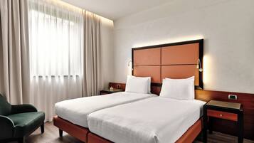 Habitación de hotel con cama doble, mesita de noche, una silla y un ventanal con cortinas.