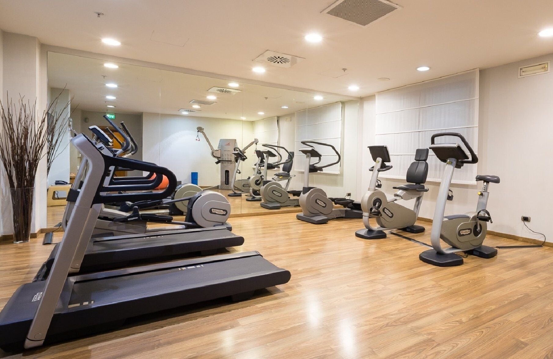 A gym with multiple exercise machines, a mirror, and a wooden floor.