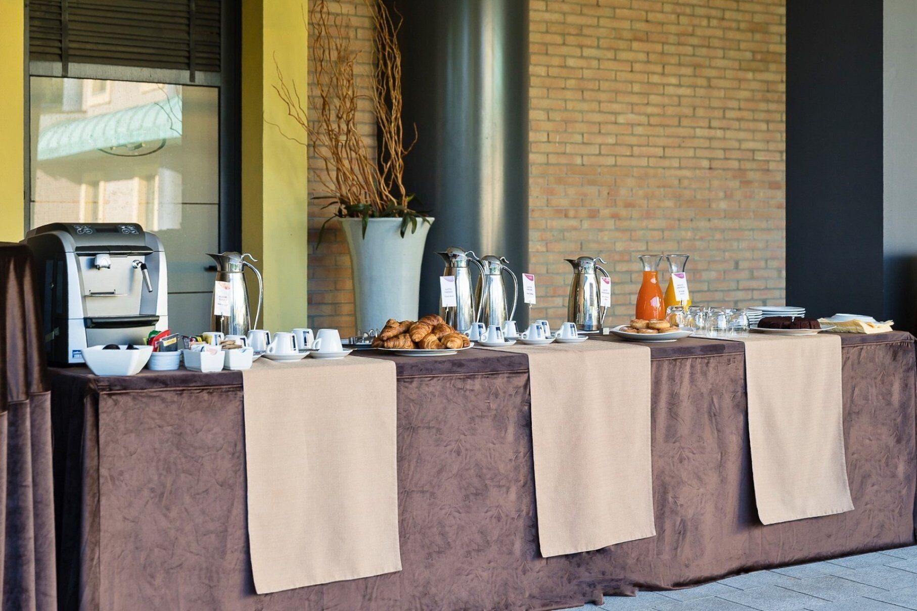 A breakfast buffet setup with coffee makers, croissants, and juice dispensers.