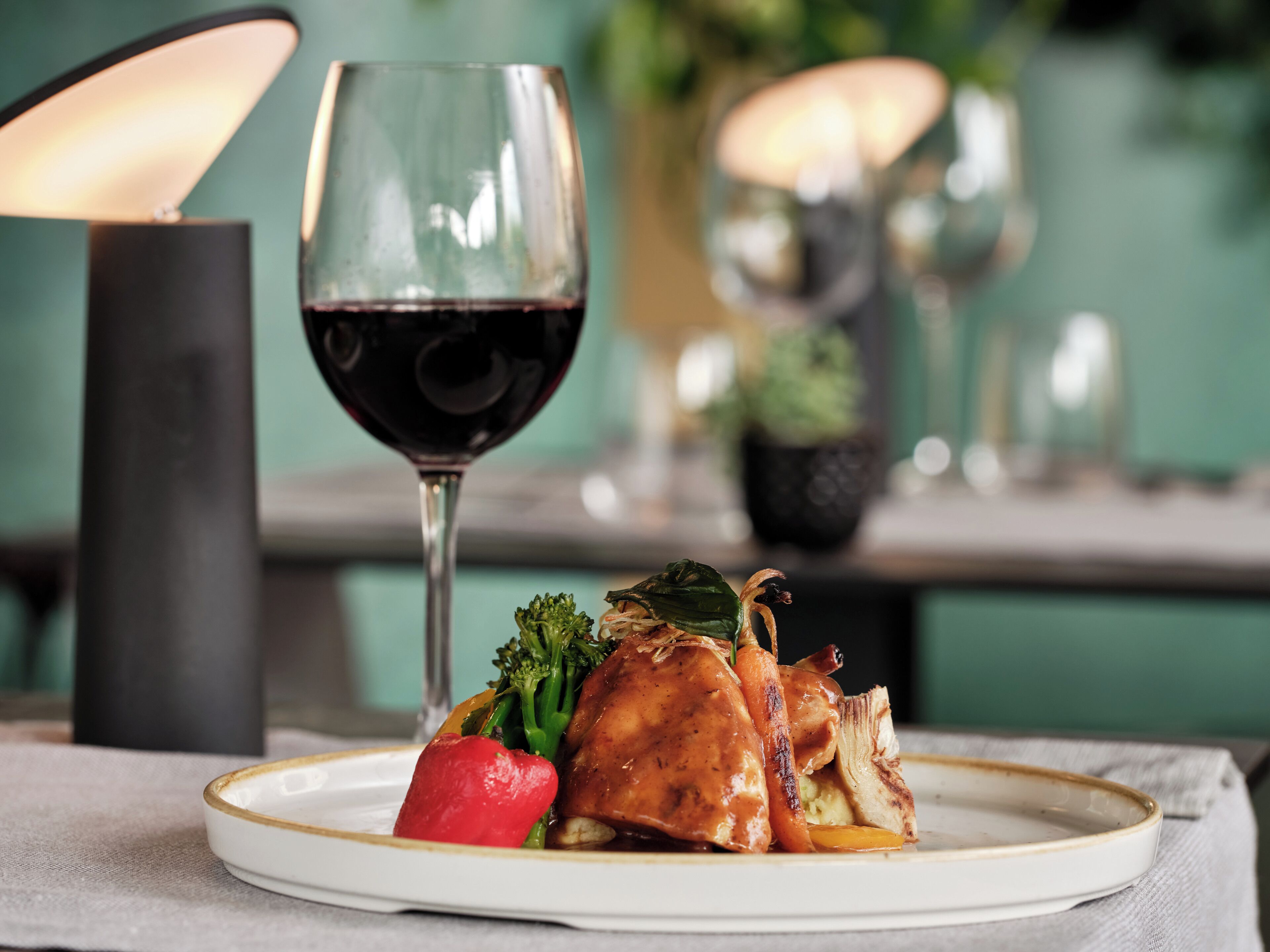 Ein Teller mit Essen, ein Glas Rotwein, eine Kerze und eine Vase mit Blumen.