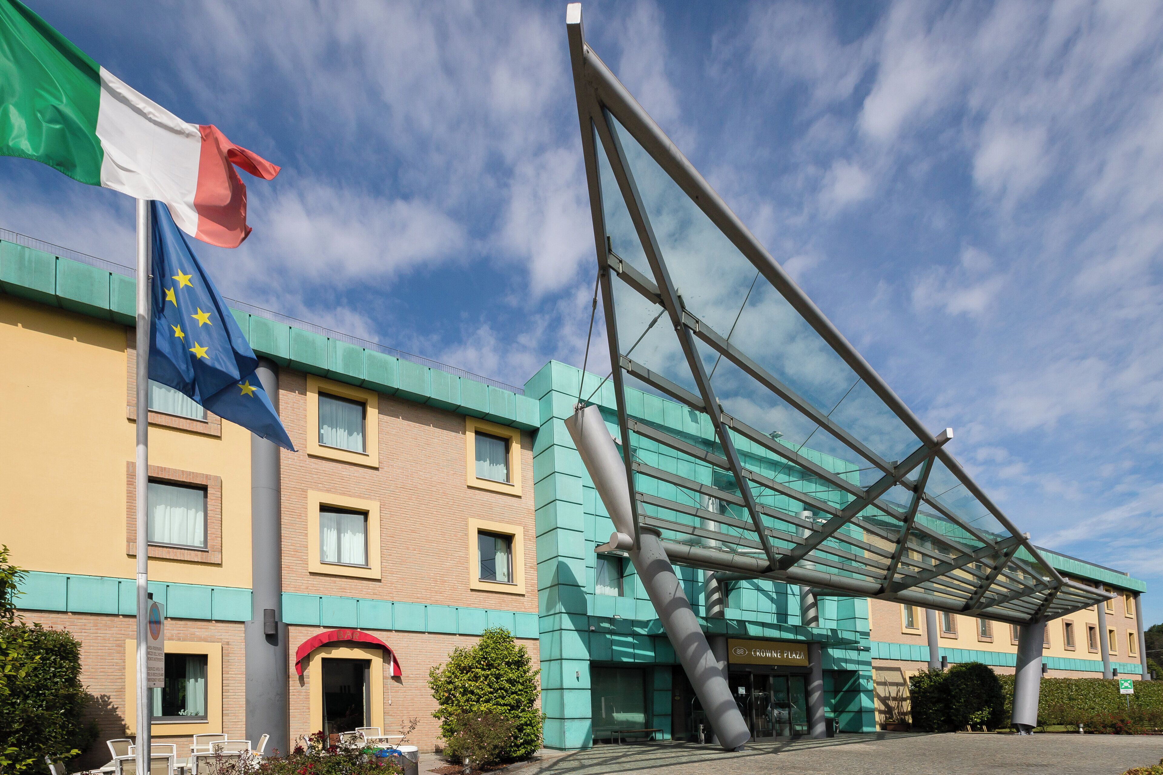 A hotel with a modern glass facade, a flagpole with multiple flags, and a clear sky.
