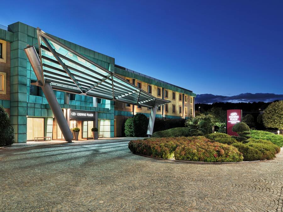 A modern hotel with a distinctive metal structure, a well-maintained garden, and a clear view of the mountains in the background.