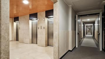 Corridoio di un hotel con ascensori, pavimento rivestito di moquette e un lungo corridoio con porte.