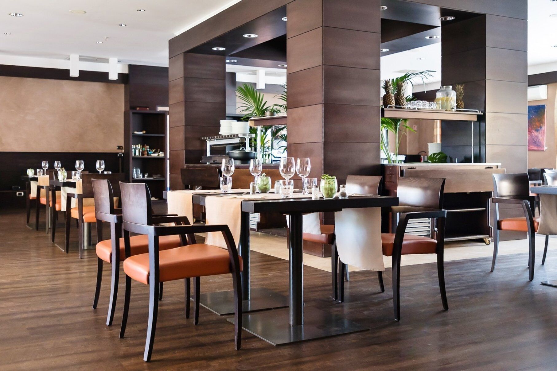 A modern restaurant with high tables and chairs, a bar area, and a view of the kitchen.
