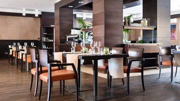 A modern restaurant with high tables and chairs, a bar area, and a view of the kitchen.