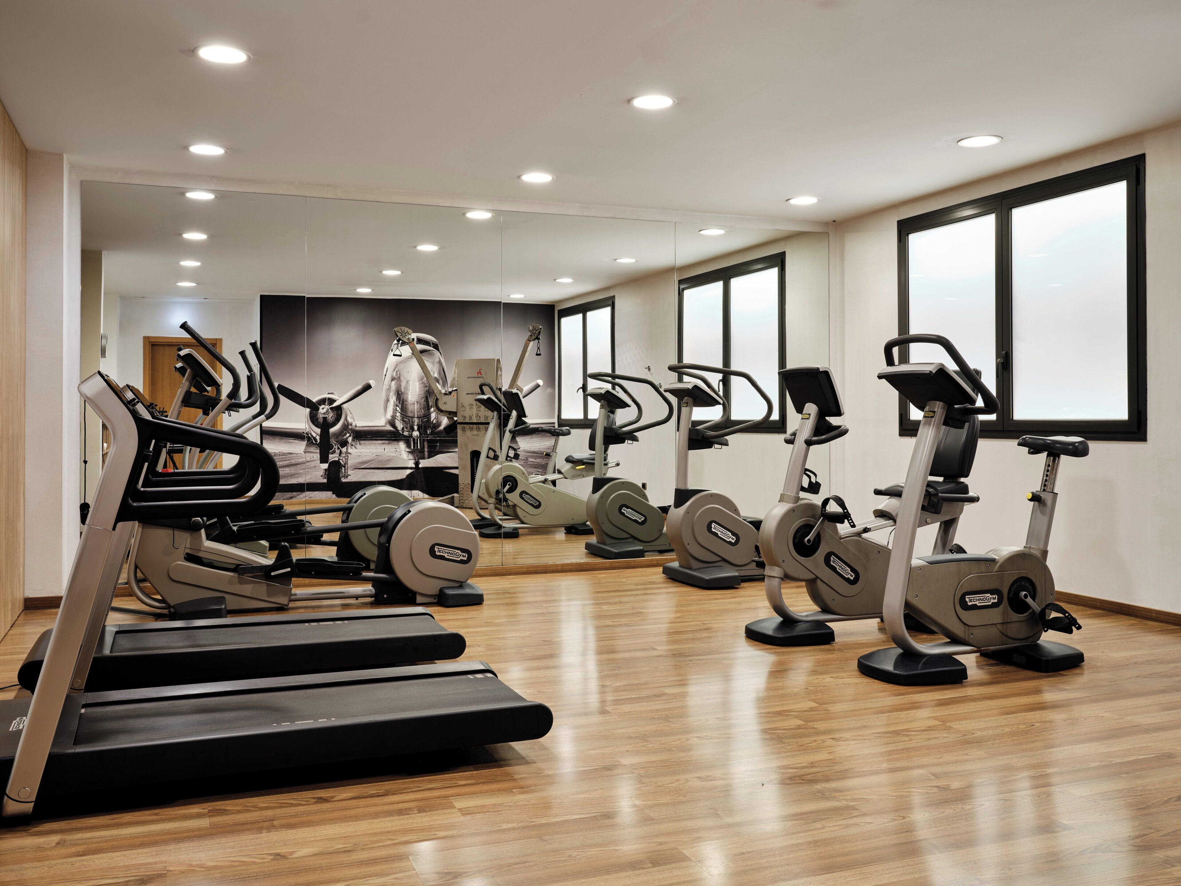 Una palestra con diverse attrezzature per esercizi, tra cui tapis roulant e cyclette, disposte in un'ampia sala con grandi finestre.