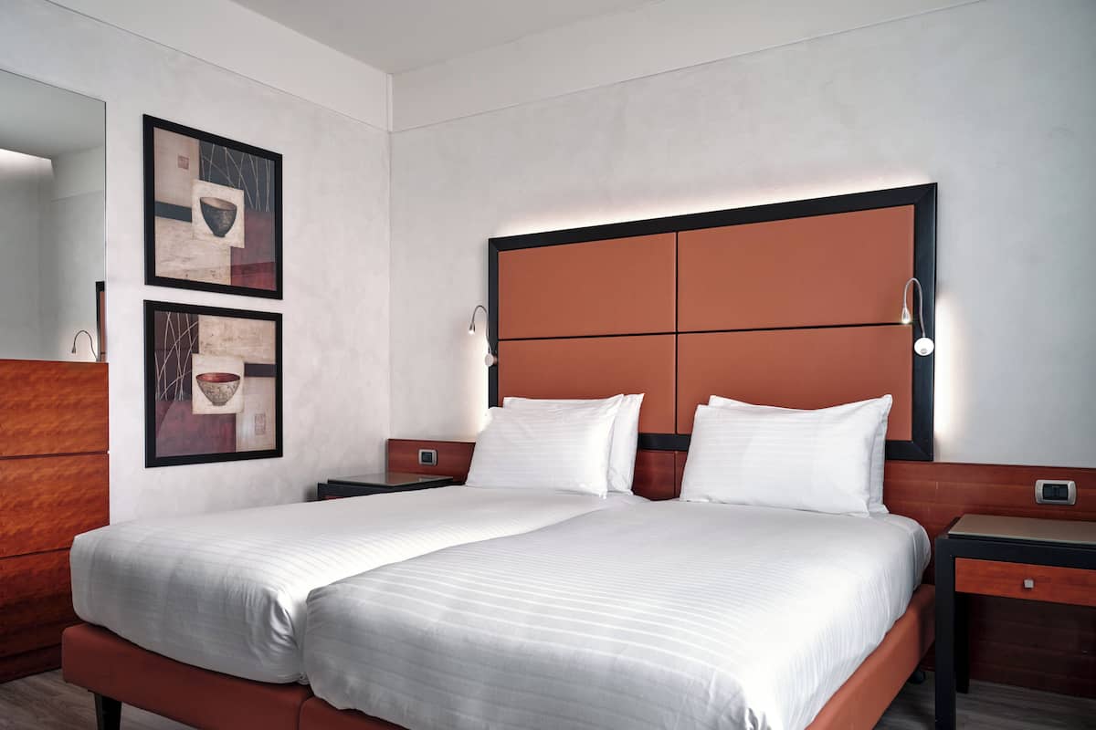 A modern hotel room with a large bed, two bedside tables, and a wooden dresser.