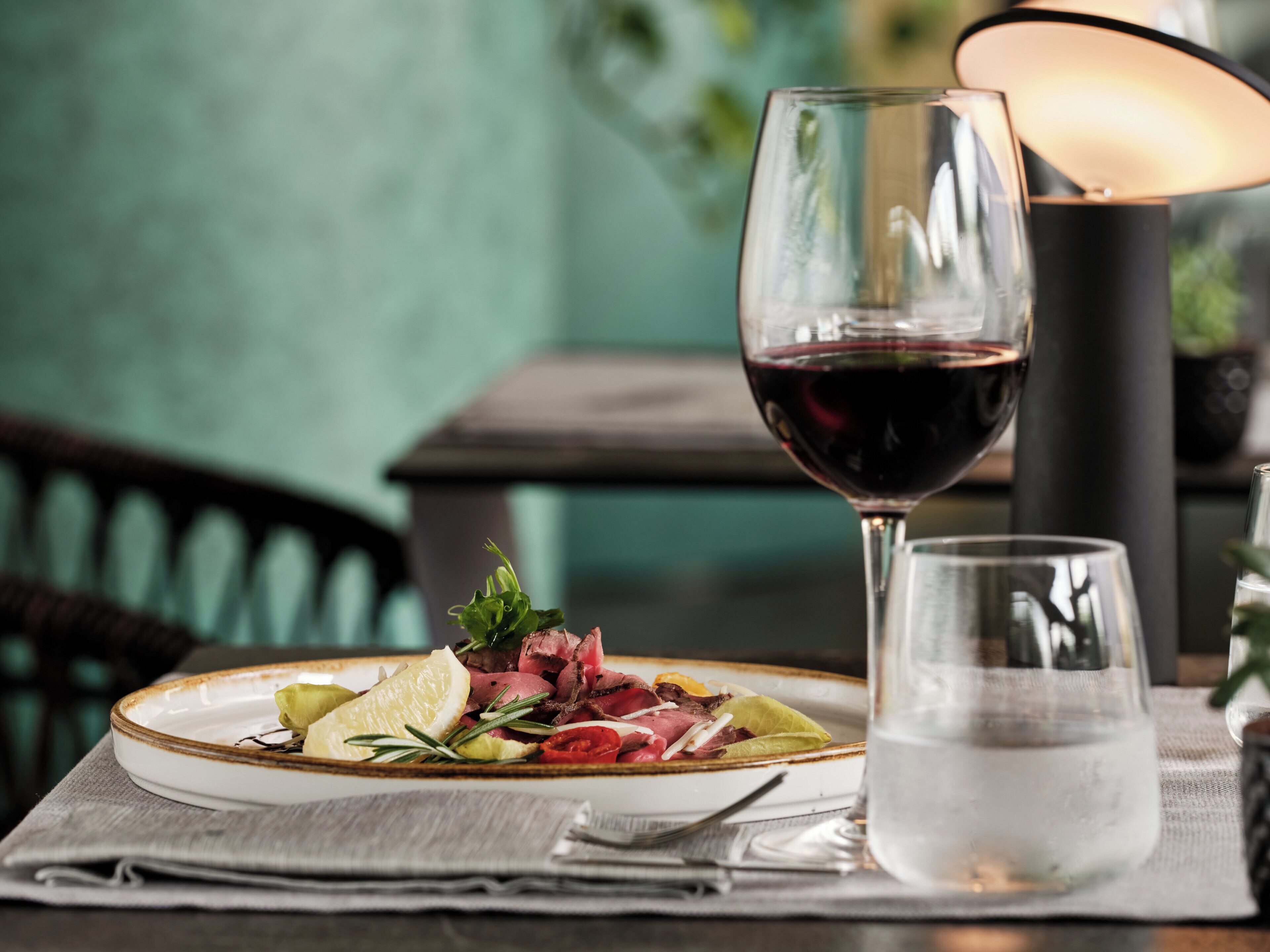 A dining table with a plate of food, a glass of red wine, and a glass of water.