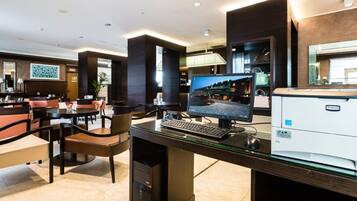 Un hall d’hôtel comprenant un comptoir d’accueil, un ordinateur, une imprimante et un espace détente avec des sièges.