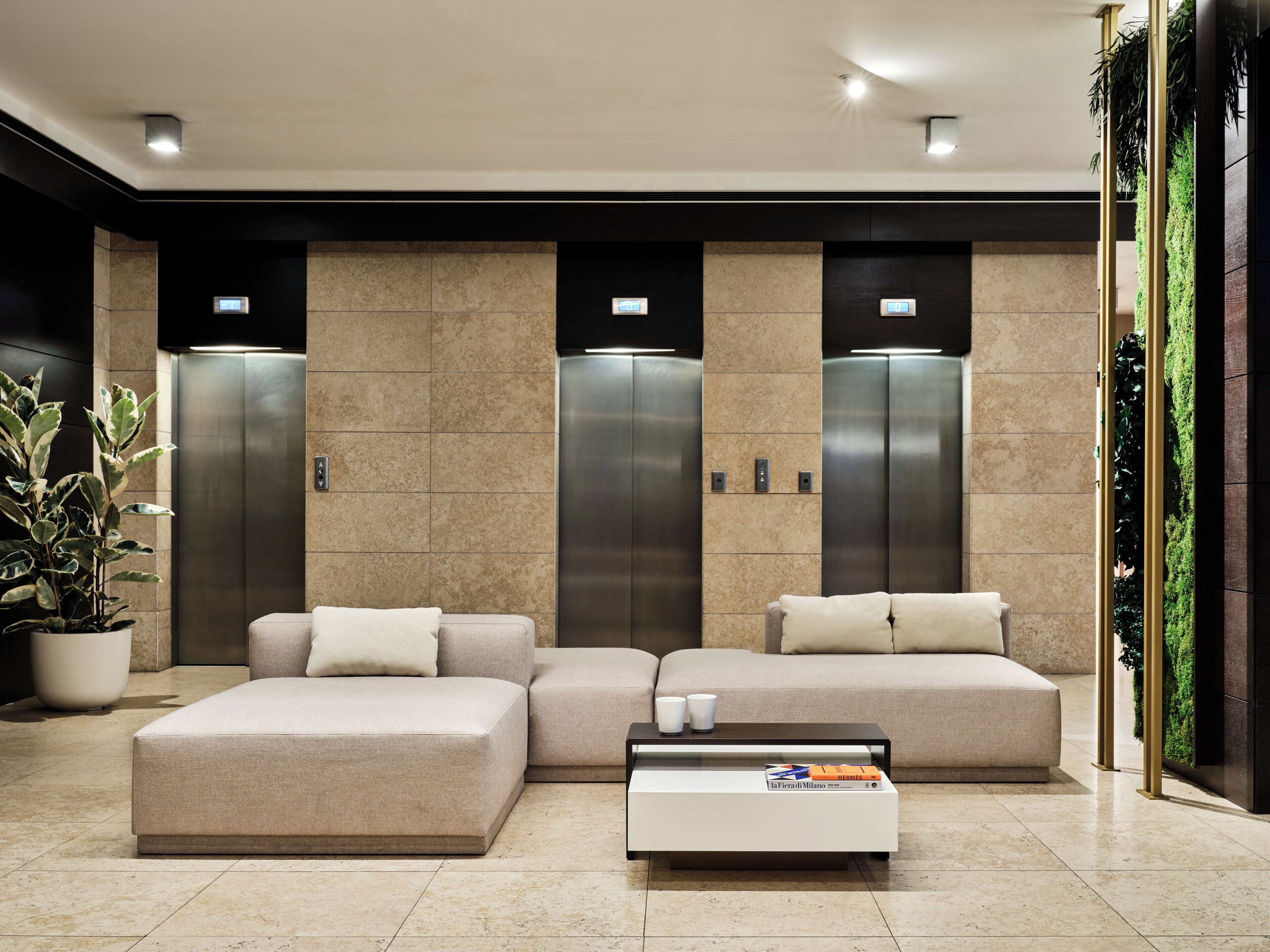 A modern lobby with a sectional sofa, a coffee table, and two elevators.