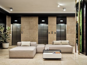Un vestíbulo moderno con un sofá modular, una mesa de centro y dos ascensores.