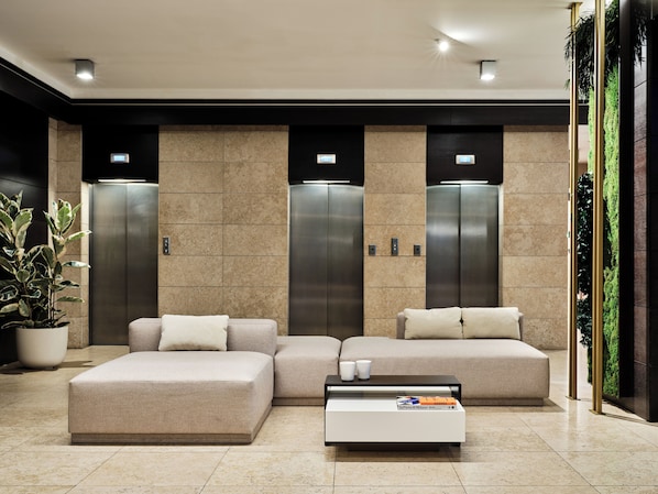 A modern lobby with a sectional sofa, a coffee table, and two elevators.