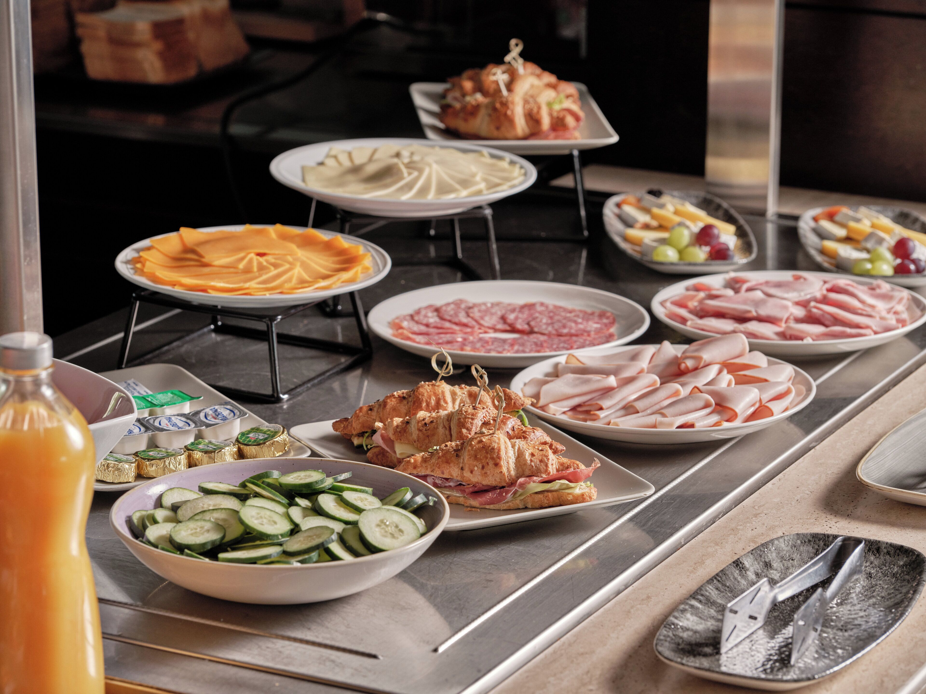 A buffet table with various food items including sliced cucumbers, ham, and a sandwich.