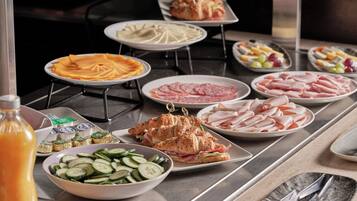 A buffet table with various food items including sliced cucumbers, ham, and a sandwich.