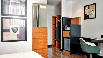 Una habitación de hotel moderna con piso de madera, un escritorio con silla, un armario y una cama.