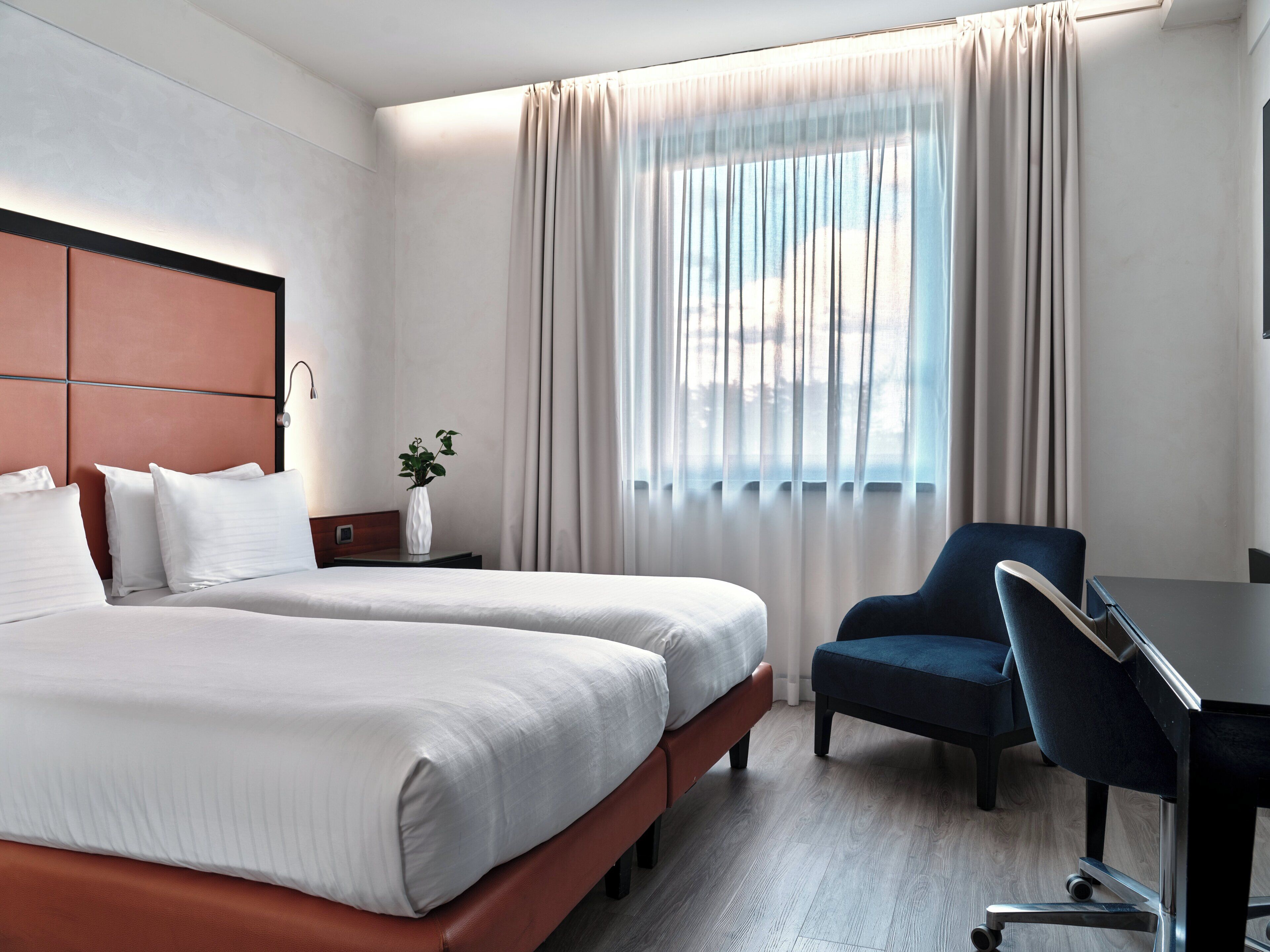 A hotel room with two beds, a desk, a chair, and a window with curtains.