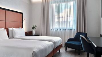 Habitación de hotel con dos camas, un escritorio, una silla y una ventana con cortinas.
