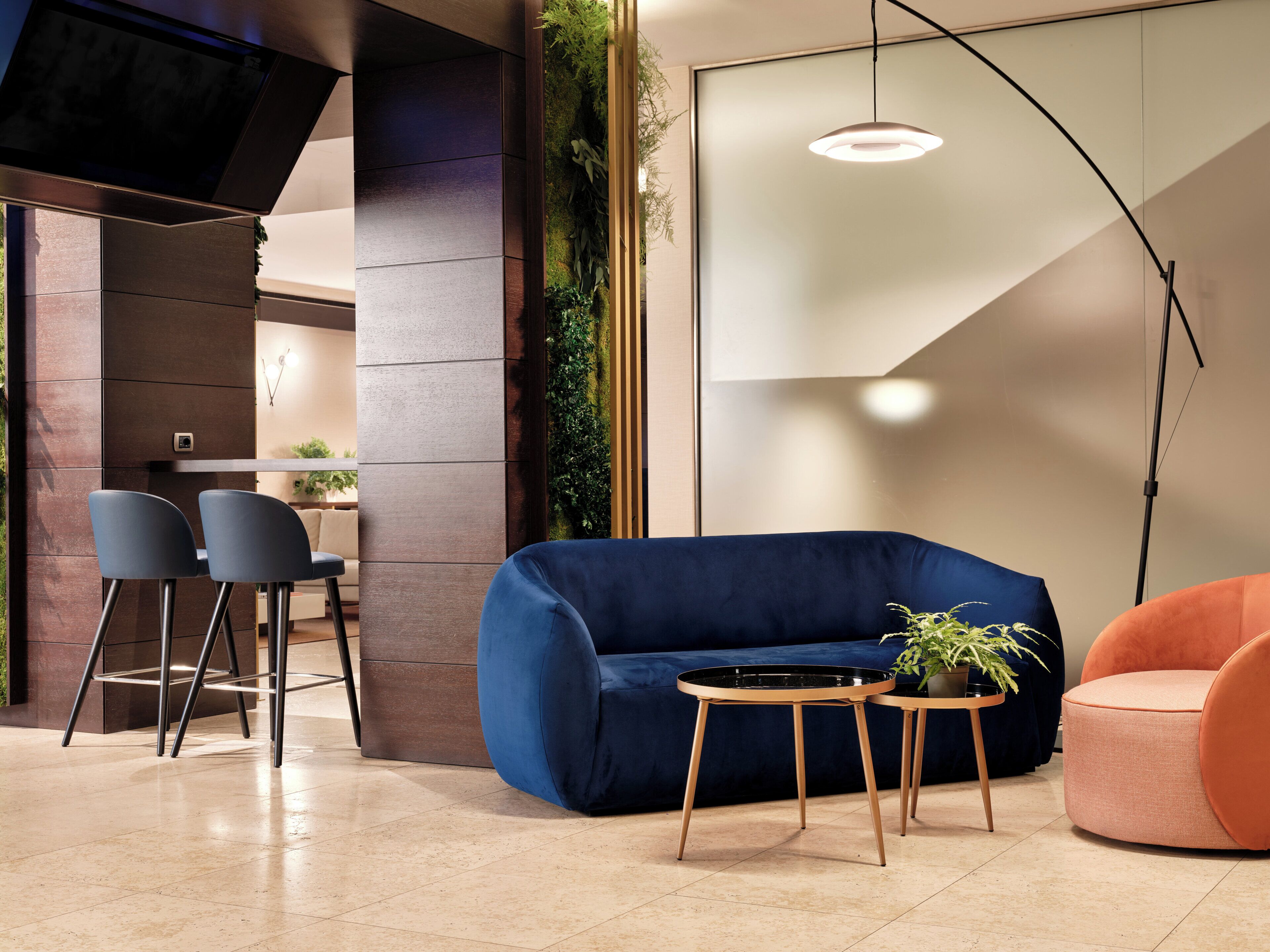 A modern living area with a blue sofa, two chairs, a small round table, and a potted plant.
