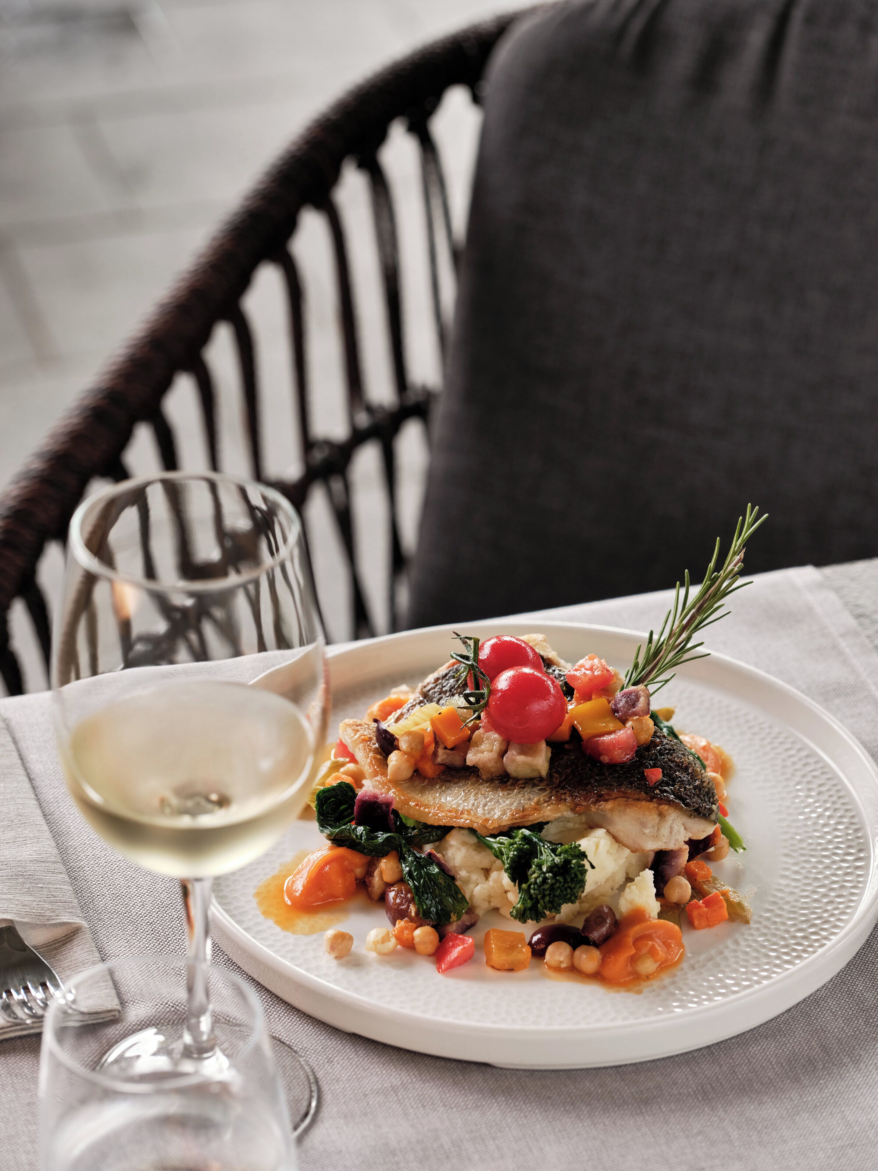 A plate of food with a glass of white wine on a table.