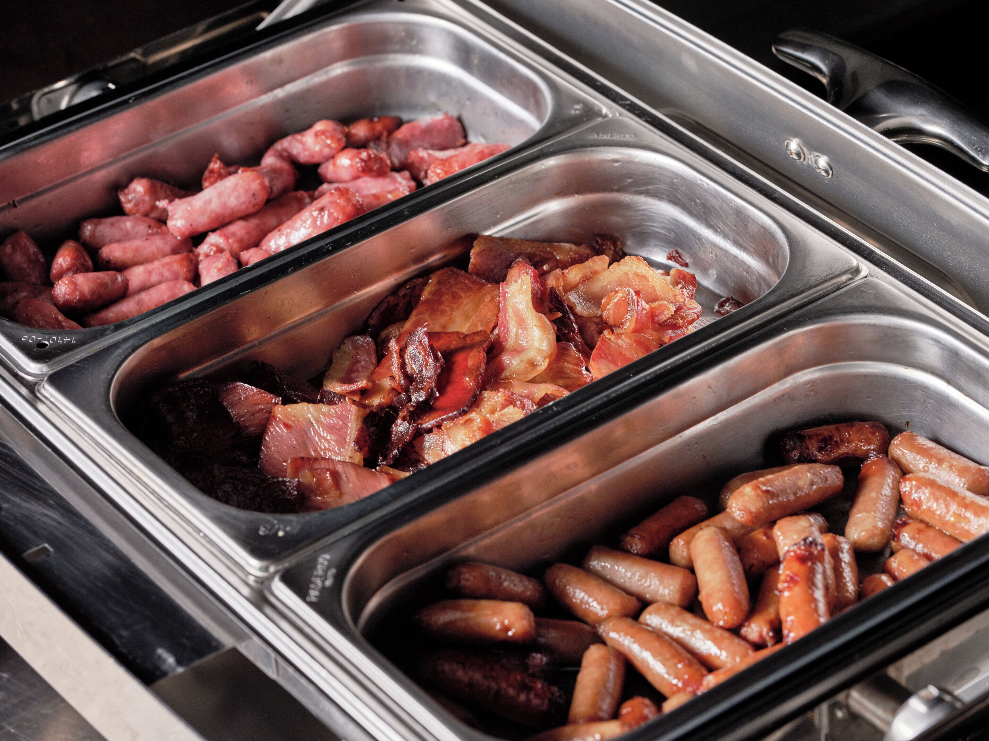 Un bufé con múltiples bandejas de acero inoxidable que contienen diversos tipos de carne cocida.
