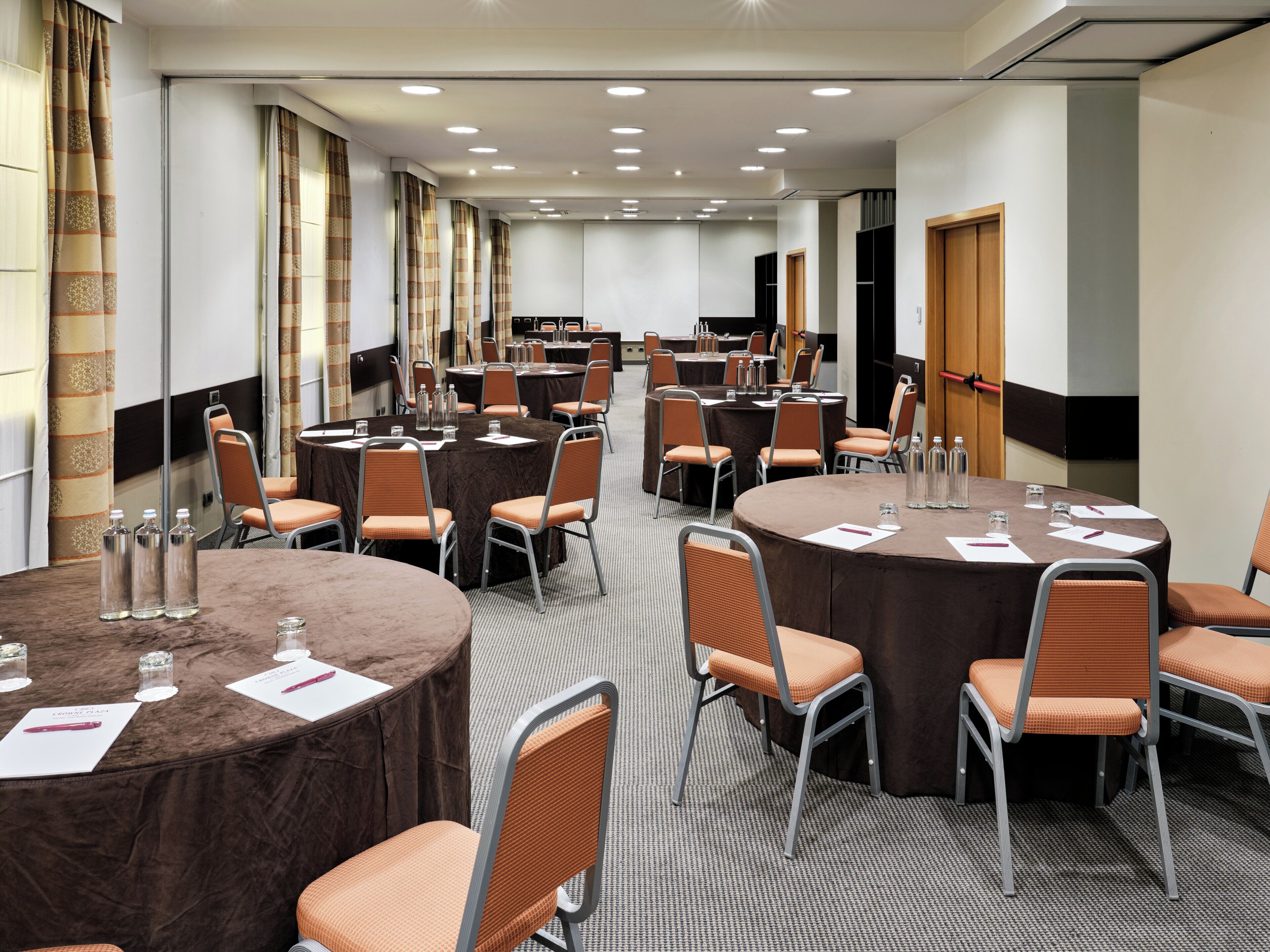 Une salle de conférence dotée de plusieurs tables et chaises, ainsi que de bouteilles d’eau et de stylos.