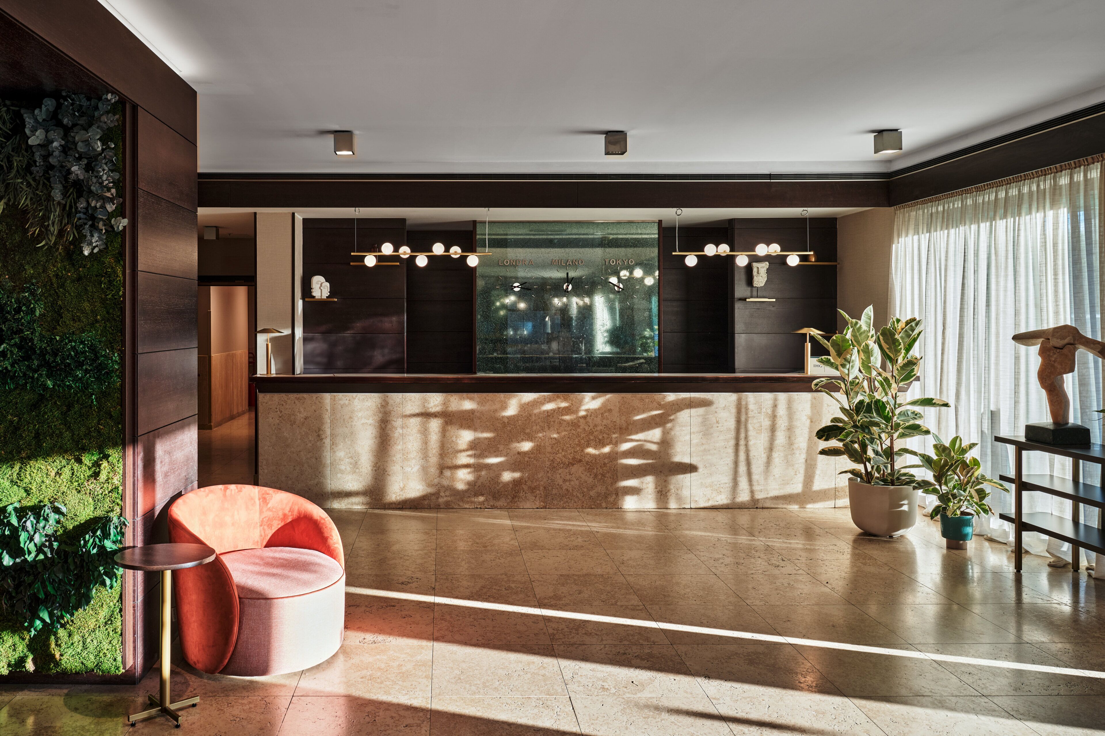 Un hall d’entrée moderne comprenant un comptoir d’accueil, un espace salon avec un fauteuil confortable et une grande fenêtre donnant sur un paysage urbain.