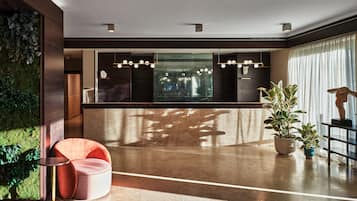 A modern lobby with a reception desk, a seating area with a cushioned chair, and a large window with a view of a cityscape.