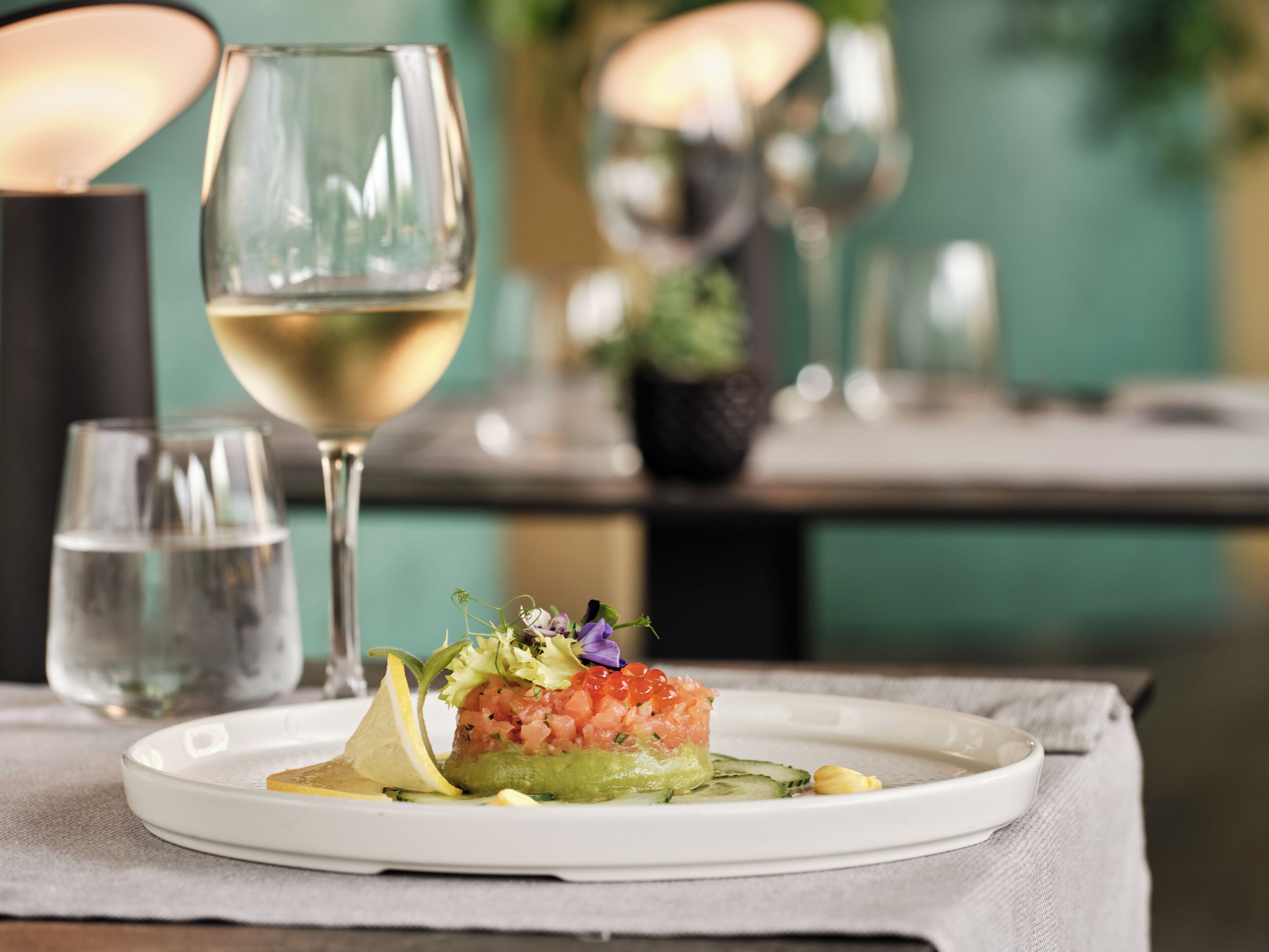Un plato de comida con una copa de vino blanco sobre una mesa.