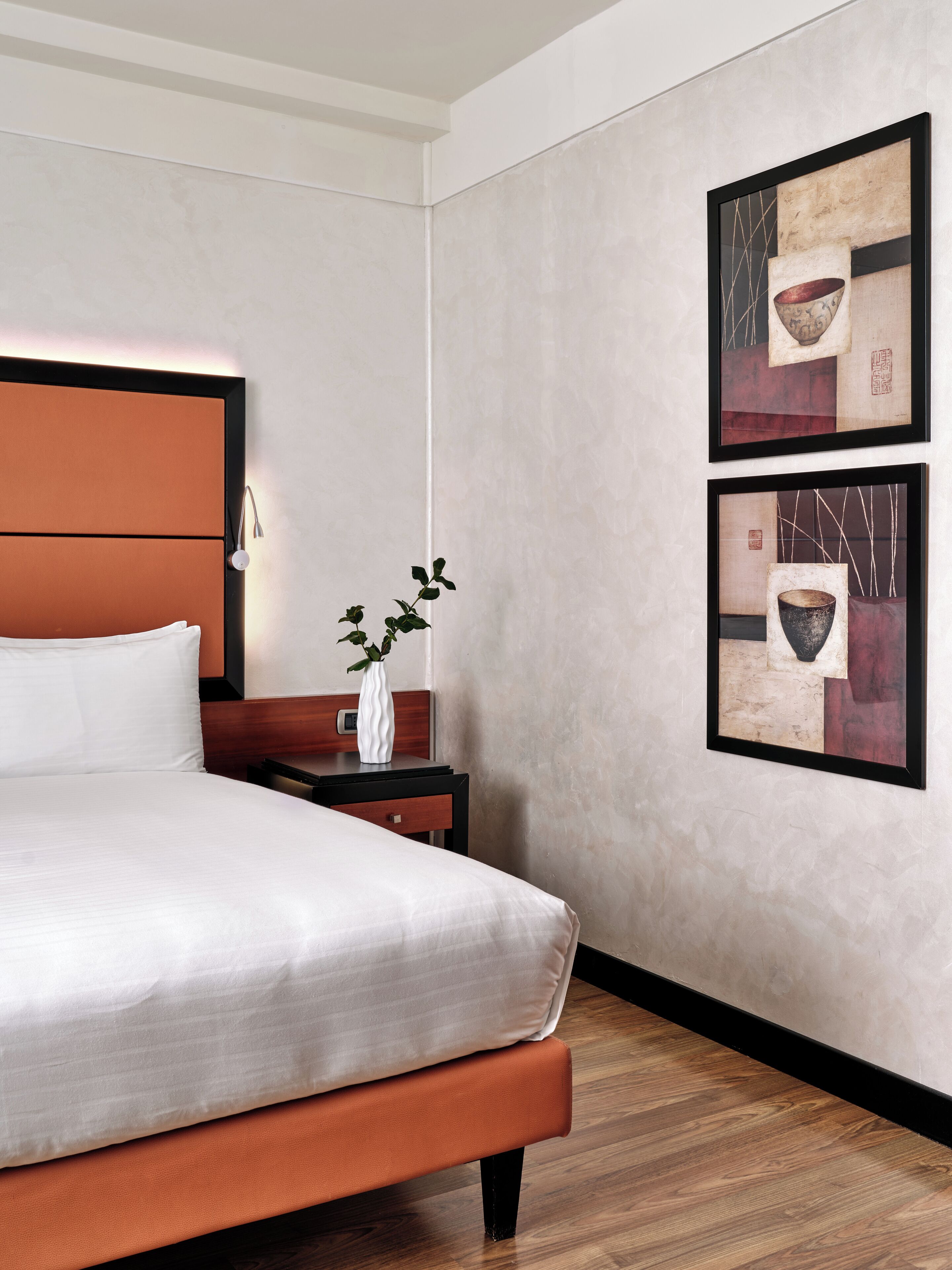 Una habitación de hotel con una cama, una mesita de noche y dos cuadros enmarcados en la pared.
