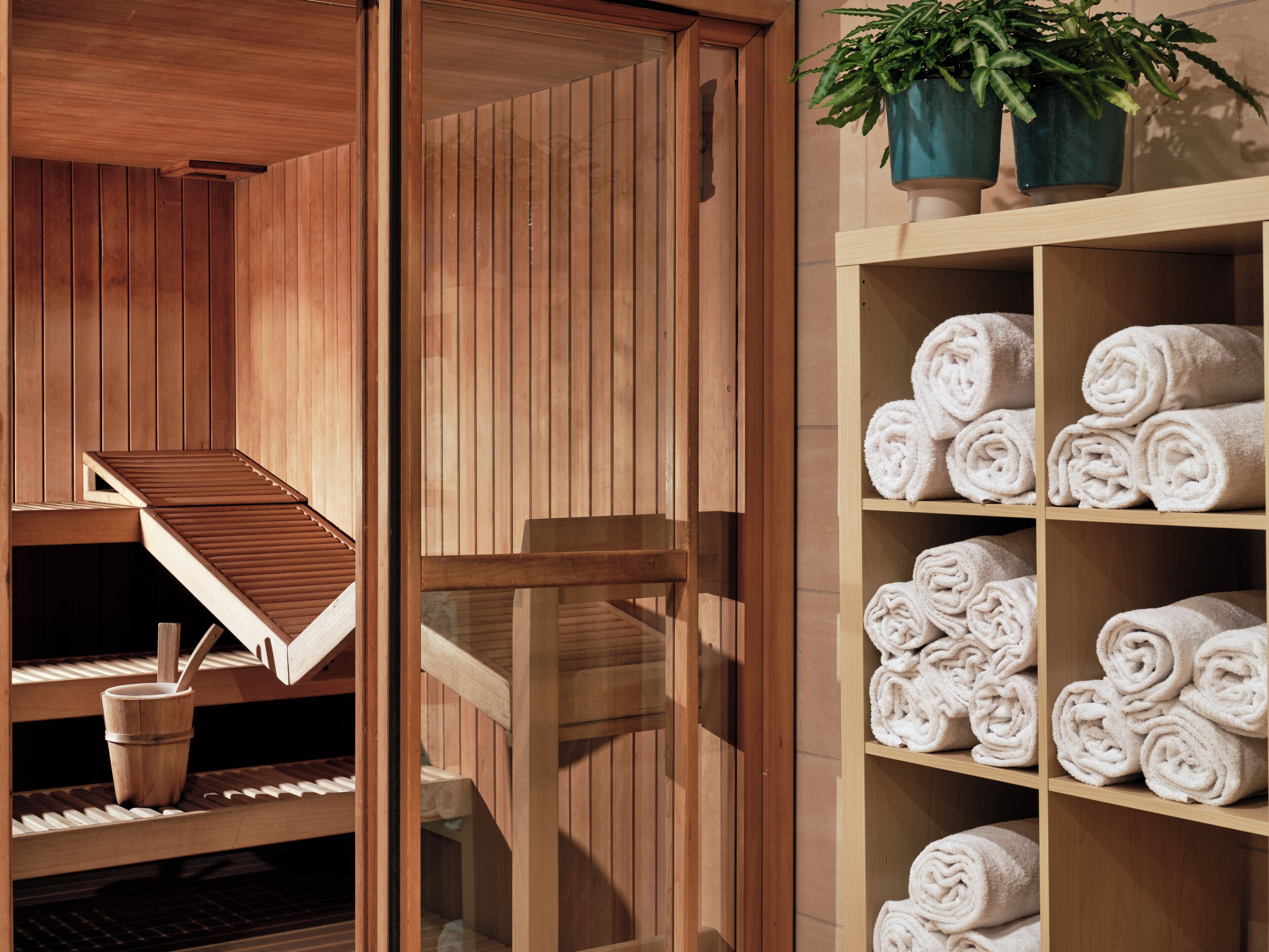 A wooden sauna with benches and a shelf of neatly rolled towels.