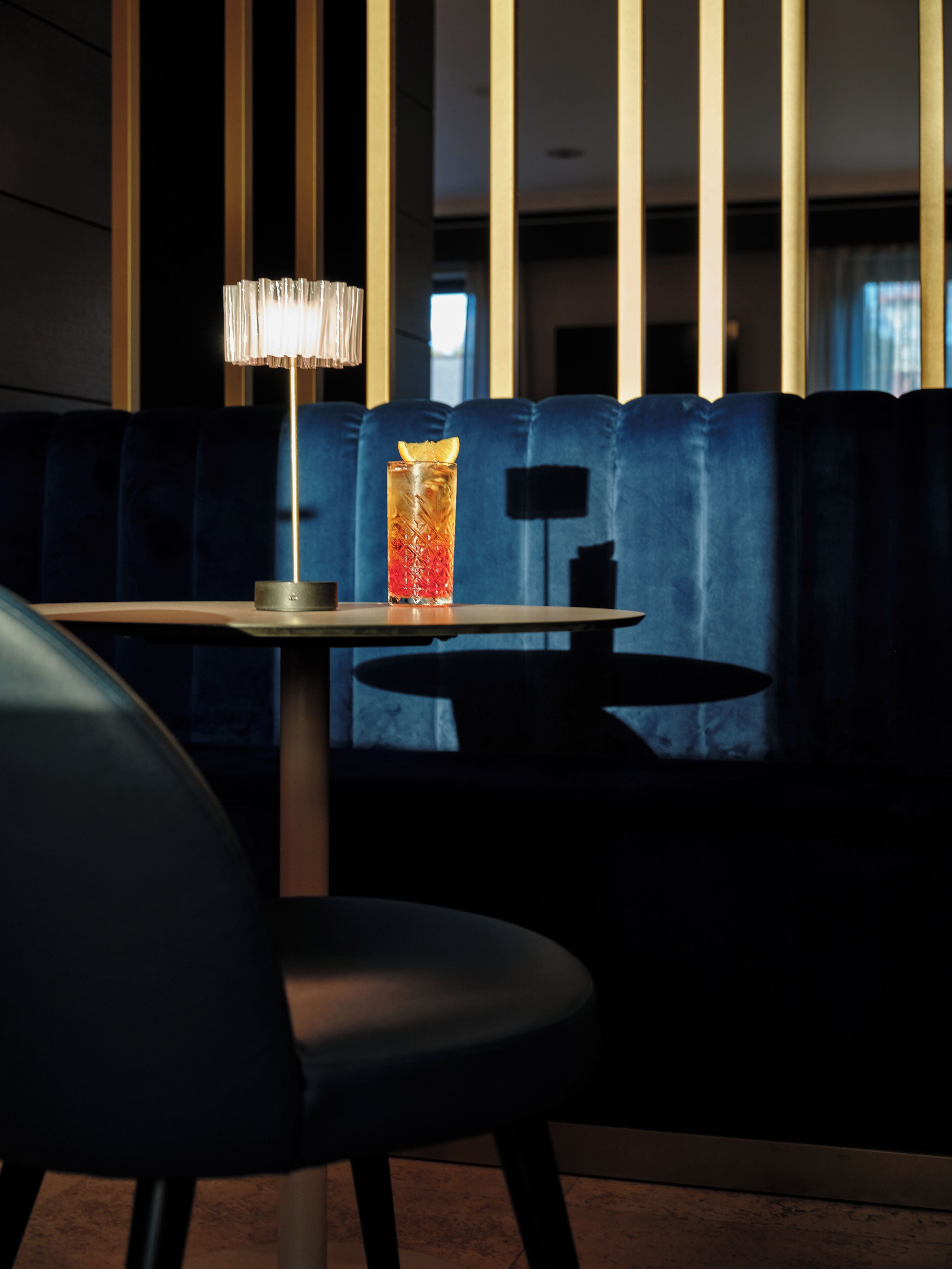 A dimly lit seating area with a table, a lamp, and a glass of drink.