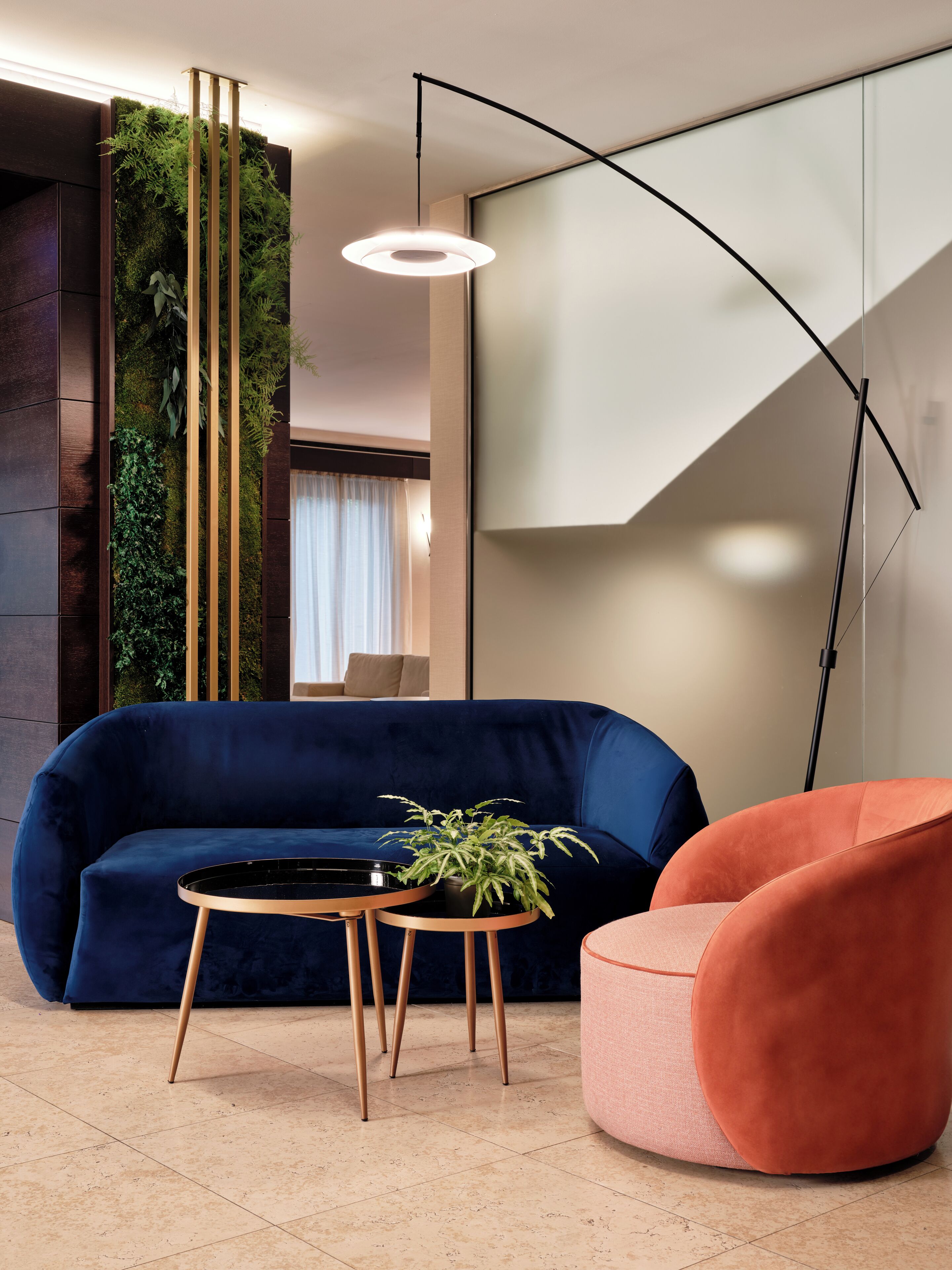 Un salon moderne avec un canapé bleu foncé, une table ronde en bois ornée d’une plante et un fauteuil rose.